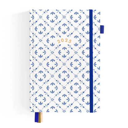 An image of a 2025 planner with white linen cover and printed blue tile pattern. Includes blue elastic band, blue pen loop and 3 ribbon markers.