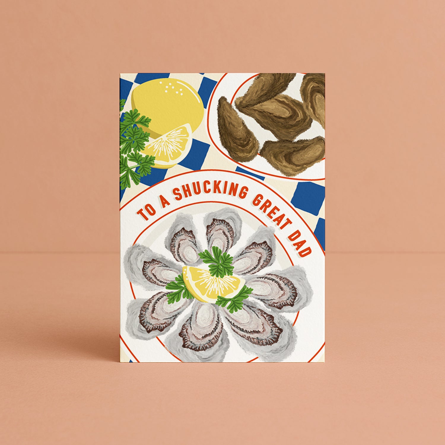 A vertical greeting card featuring an illustration of oysters and lemons, with the text 'TO A SHUCKING GREAT DAD' in red lettering curved around the edge of the plate, photographed standing against a solid peach background. 